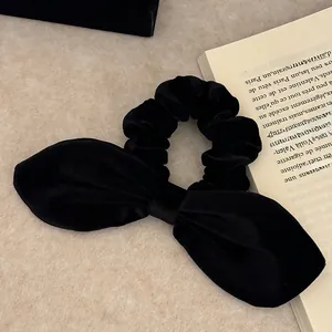 French style black velvet hair scrunchie with a large bow on a textured background