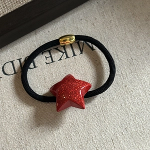 Detail of a red glitter star hair tie with black elastic band and gold metal connector