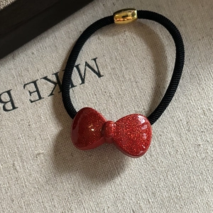 Detail of red glitter bow hair tie with black elastic band and golden metal buckle