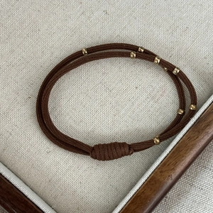 Brown dual-strand elastic hair tie with gold beads on grey linen background