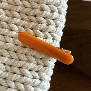 Close-up of a glossy orange rectangular hair clip with a gold metallic duckbill base