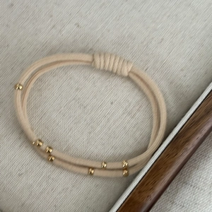 Macro detail of beige elastic hair tie with polished gold metallic cylinder beads