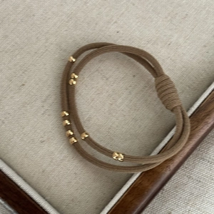 Detail of coffee brown elastic hair tie featuring golden decorative beads on fabric background