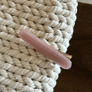 Close-up of a pale pink resin hair clip with a gold metal base on woven texture