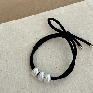 Détail de l'élastique à cheveux noir avec trois perles blanches et embouts dorés