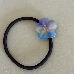 Elastic hair tie featuring a colorful gradient flower charm with gold Barrette lettering