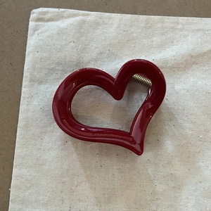Dettaglio di una pinza per capelli a forma di cuore rosso lucido con molla in metallo dorato