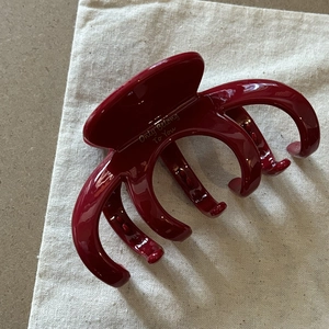 Dettaglio della grande molletta per capelli rossa con scritta dorata su sacchetto di lino