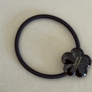 Close-up of elastic hair tie featuring a dark brown acetate flower with gold lettering