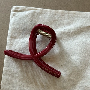Dettaglio della grande molletta per capelli bordeaux con scritte dorate su sacchetto di cotone