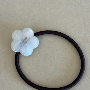 Macro shot of white acetate flower with pearlescent finish on black elastic hair tie