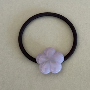 Close-up of a purple acetate flower hair tie with golden lettering and elastic cord