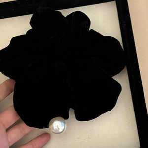 Detailed view of a black velvet scrunchie with an elegant white pearl accent