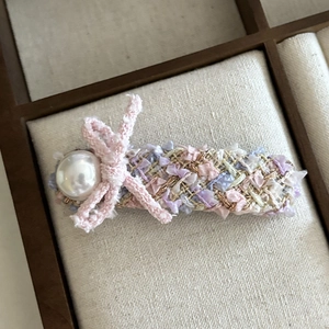 Elegant pink tweed bow hair clip with large pearl accent on wood and linen background