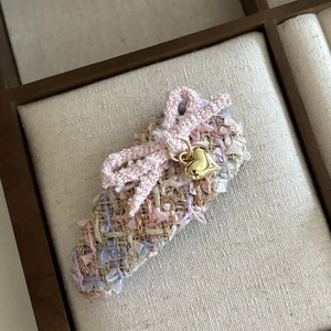 Detailed macro view of a pink tweed bow hair clip with a golden heart charm