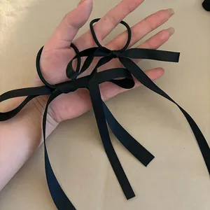 Detailed view of two handmade black satin bow hair ties held in hand against a beige table
