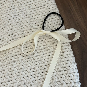 Elegant cream satin bow hair tie with black elastic band on a warm wooden background