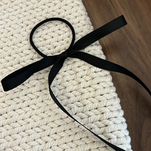 Elegant black satin ribbon bow hair scrunchie shown on a minimalist white knit surface