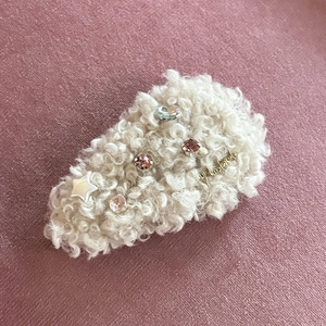 Détail de la barrette en peluche crème avec strass roses et un accent de logo doré
