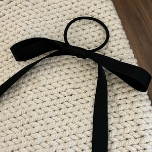 Close-up of a black satin ribbon bow hair tie on a beige woven textured background