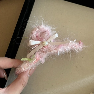 Detail of pink plush claw clip with silk bow and pearl accent on beige tray