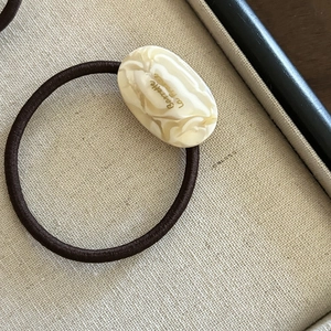 Détail macro d'un élastique à cheveux crème marbré avec lettrage doré chic