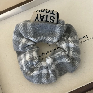 Close-up of a grey plaid fabric scrunchie with a Stay Today woven label on text background