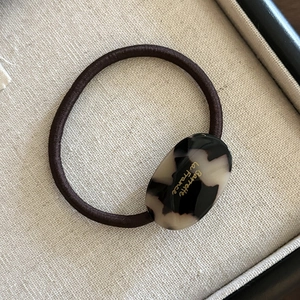 Détail de l'élastique à cheveux avec boucle ovale en écaille ambrée et lettrage doré