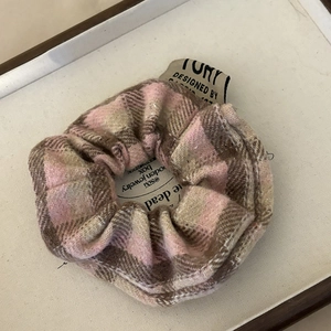 Close-up of a pink and brown plaid oversized scrunchie with a woven tag in a white box