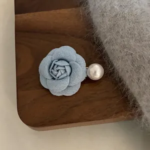Pince à cheveux camélia en tissu bleu clair avec perle sur un plateau en bois sombre