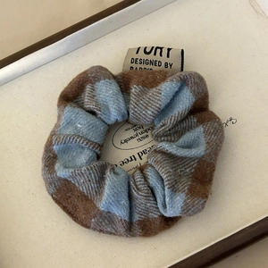 Detail of blue and brown plaid plush scrunchie with a woven label in a wooden box