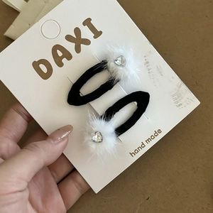 Close-up of black bow hair clips with white fur balls and heart rhinestones on card