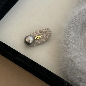 Close-up of beige tweed hair clip with grey pearl and engraved gold metal heart charm