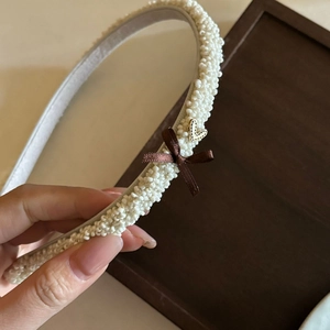 Détail d'un serre-tête en perles avec un nœud en ruban marron et un cœur doré poli