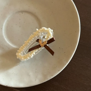 Détail d'une pince à cheveux avec nœud en satin marron, perles et petit cœur doré