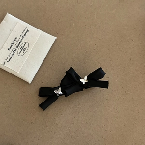 Detail of a black ribbon bow hair clip with silver butterfly charms on a neutral backdrop