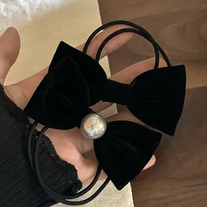 Détail de deux chouchous nœuds en velours noir avec perle devant un fond en dentelle