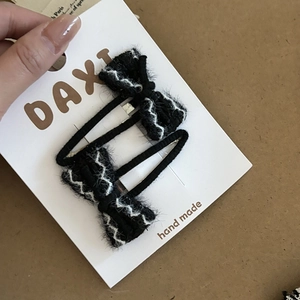 Detail of two black tweed bow hair clips with white zigzag stitching on display card