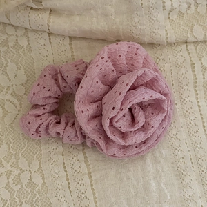 Pink eyelet fabric rose scrunchie with intricate hollow texture on vintage lace background