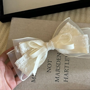 Detail of layered cream silk bow hair clip with lace and organza on a book
