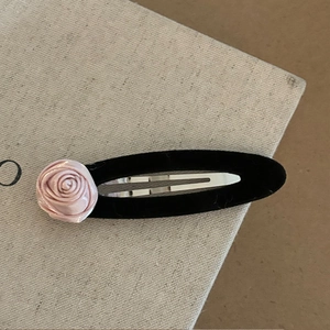 Barrette à fleur rose en satin avec base en velours noir sur une surface beige texturée