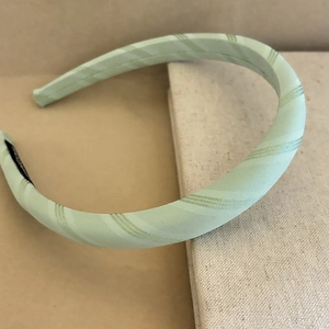 Light green fabric headband with elegant diagonal stripes on a textured background
