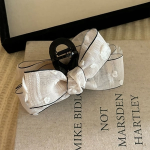 Detailed close-up of white polka dot silk ribbon bow hair claw clip with black edging
