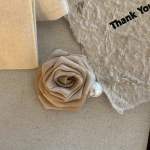 Elegant champagne gold fabric flower hair claw with white pearl detail on linen background