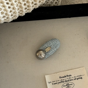 Blue tweed pearl hair clip with gold metal tag and silver sphere accent on canvas