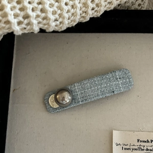 Macro detail of baby blue tweed hair clip with pearl bead and gold 'White' charm