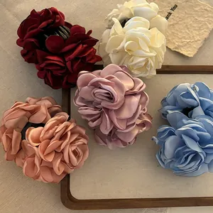 Detail of multi-color 3D satin rose hair claws with elegant silk texture on wooden tray