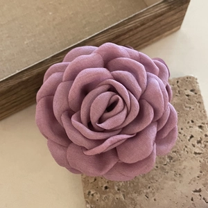 Macro shot of a handmade 3D fabric rose hair clip in pink purple on a stone tray