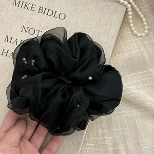 Close-up of fluffy black organza scrunchie with pearls held against linen bag background