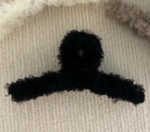 Détail d'une grande pince à cheveux noire avec dentelle plissée sur surface en maille beige
